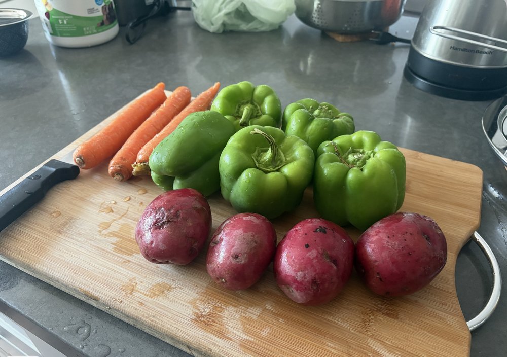 Red potatoes, carrots, and green bell peppers on a cutting board
