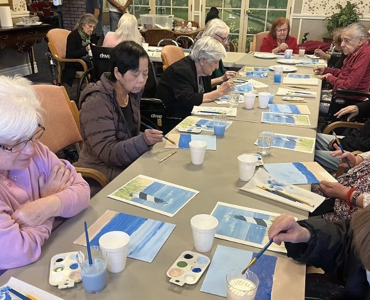 Residents painting along a long table with blue seaside paintings in progress