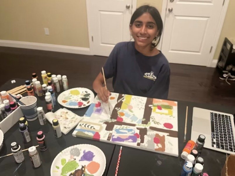 A CARES officer painting at a table surrounded by paint bottles and palettes