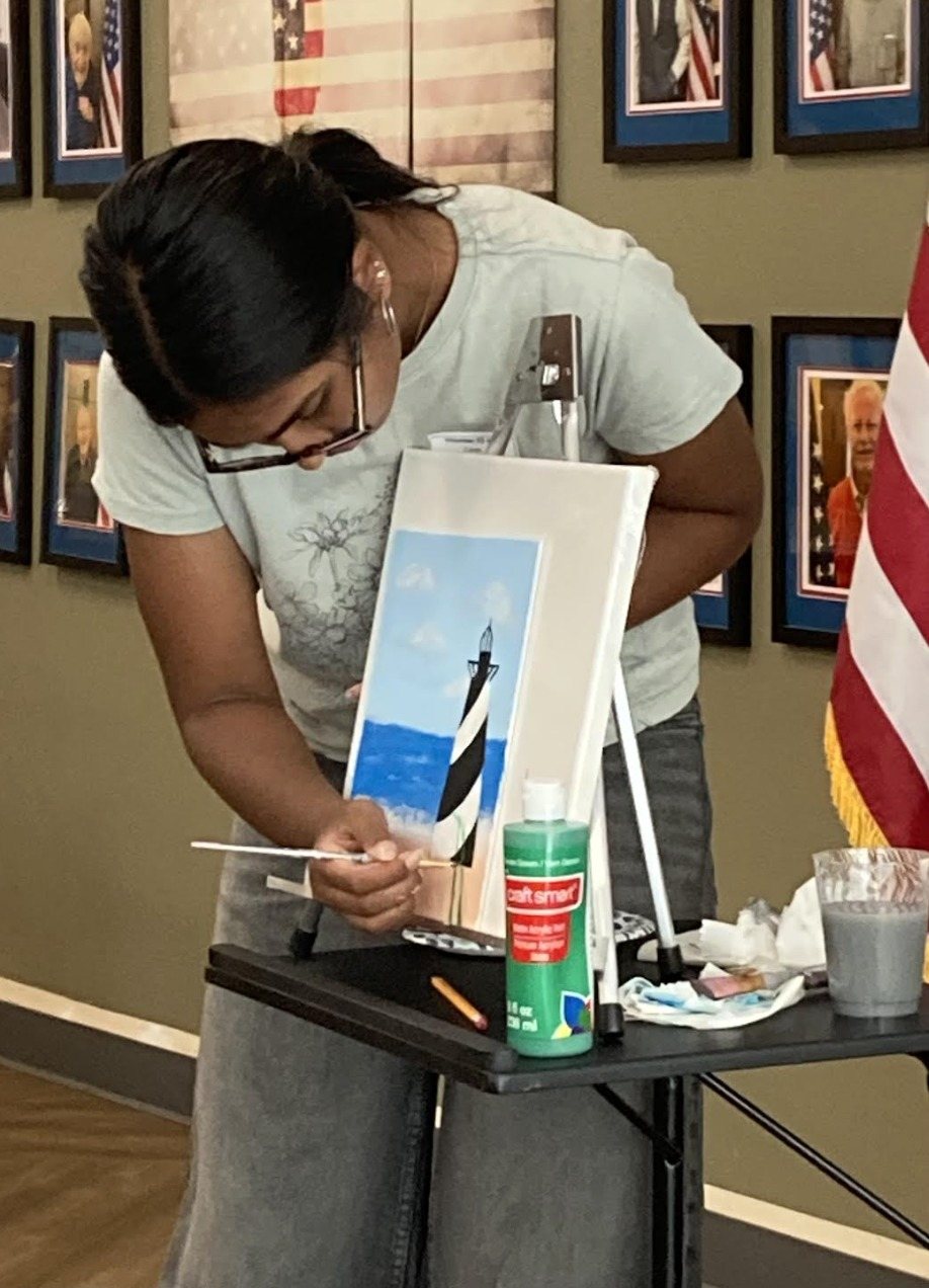 A CARES officer helping at an easel with a lighthouse painting