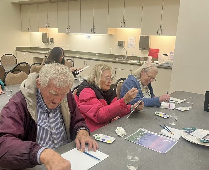 Residents painting at a table with a lavender moon painting as their guide