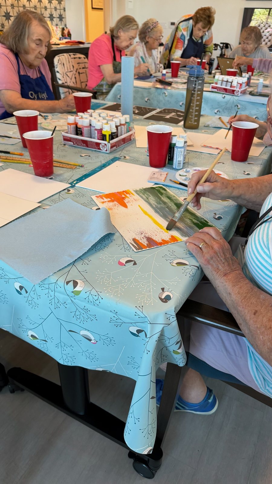 Residents painting at a table with cups of paint and brushes