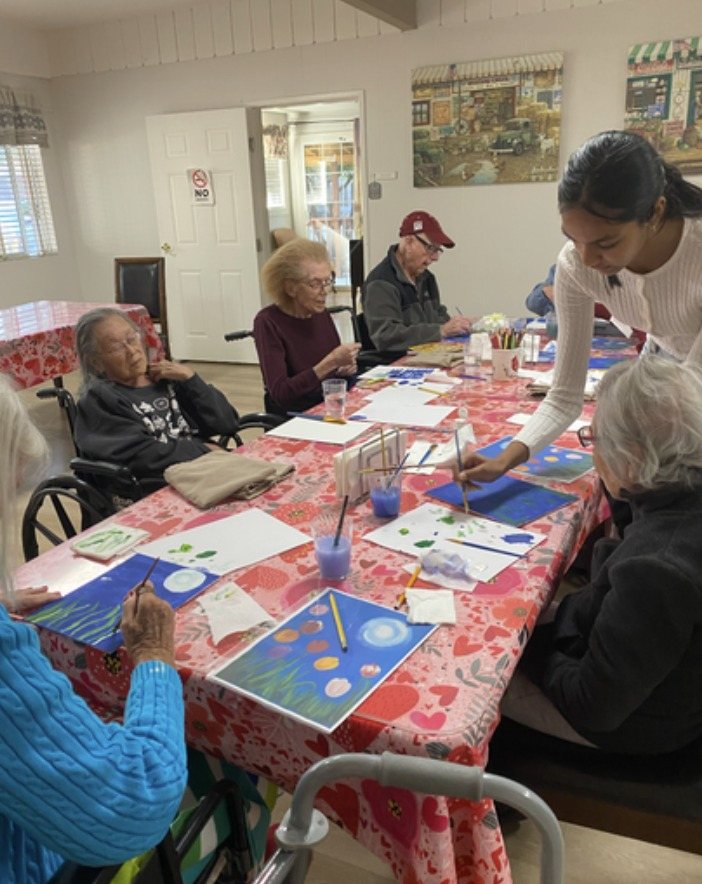 A CARES officer helping residents paint a night scene with glowing orbs at a table