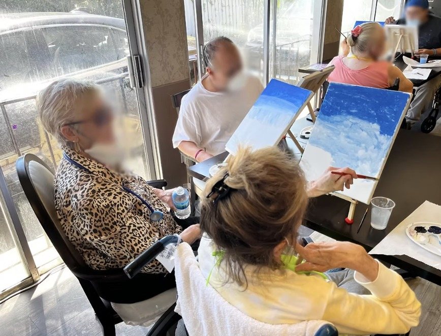 Residents painting skies on easels by a sunny window