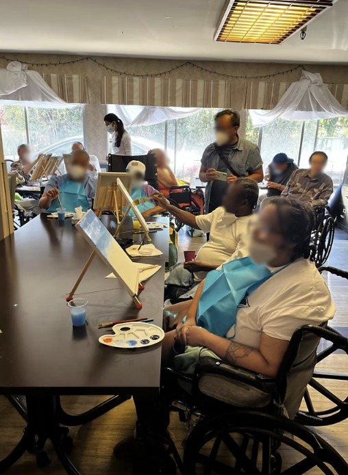 Residents painting at easels while volunteers help