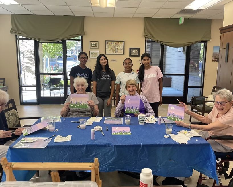CARES volunteers standing behind seniors who hold up their moon paintings
